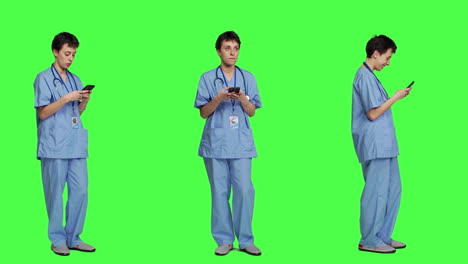 Young-nurse-texting-on-smartphone-against-greenscreen-backdrop